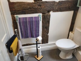 Un baño con inodoro blanco, toallero con toallas y un rollo de papel higiénico.