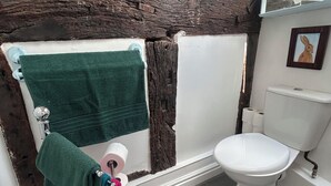 A bathroom with a white toilet, a green towel, and a wooden beam ceiling.