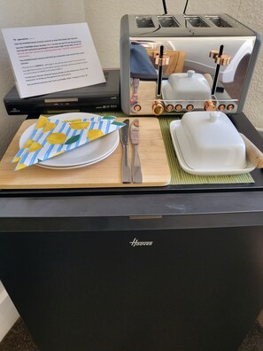 Una encimera de cocina con un tostador, un plato con servilleta de estampado de limón, un cuchillo y un recipiente blanco.