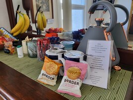 Una presentación de desayuno con tetera, bolsitas de té, café, fruta y aperitivos envasados.