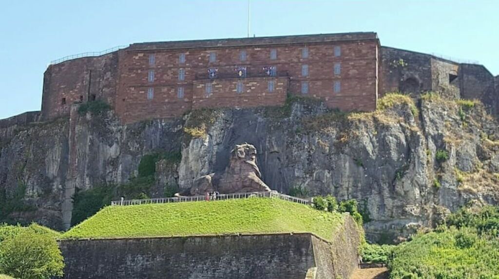 Un gran edificio de ladrillo con una estatua sobre un montículo de césped.
