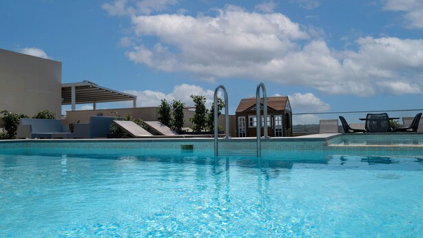 Una piscina con agua azul cristalina, sillas de descanso y un edificio con techo de tejas al fondo.
