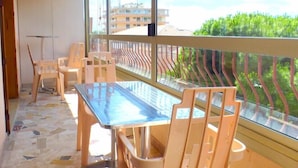 Ein Balkon mit Glastisch und Stühlen, Blick auf Gebäude und Grünflächen, und ein Fliesenboden.