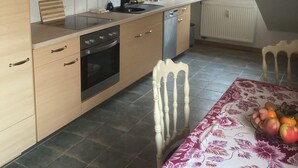 A modern kitchen with wooden cabinets, a built-in oven, and a dining area with a table set for two. - Immensee I Apartment with lake view surrounded by forest (Ronshausen)