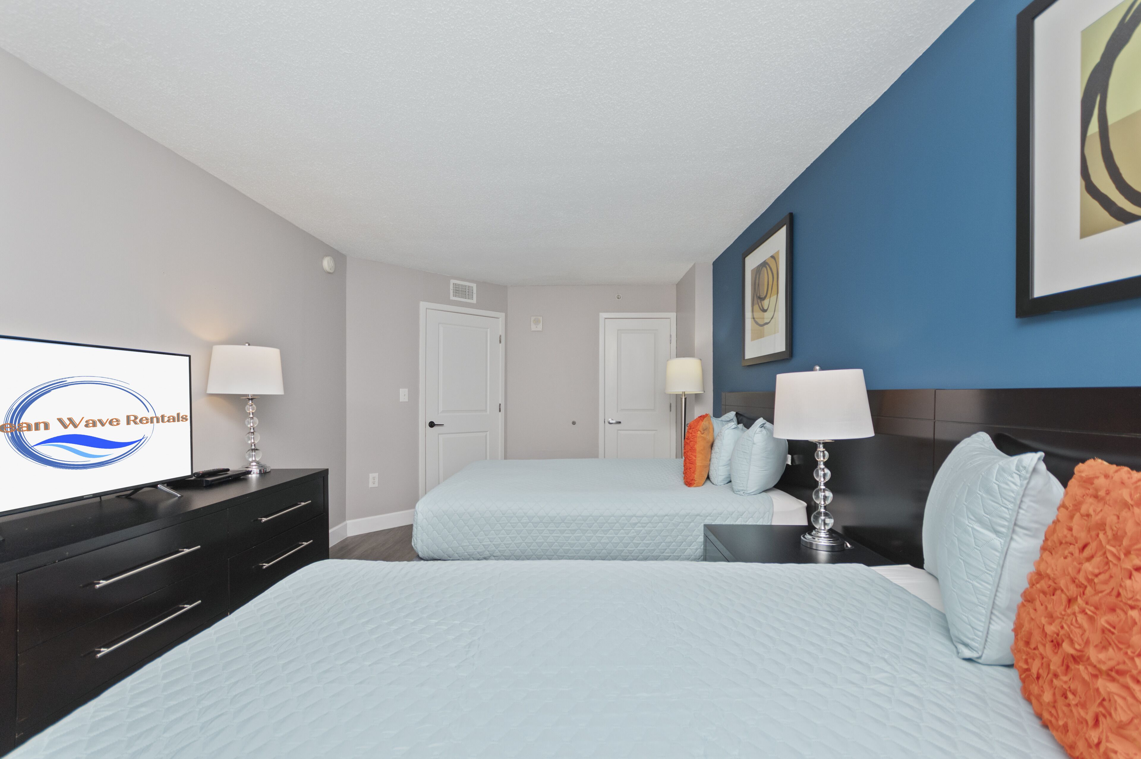 Une chambre d’hôtel avec deux lits, une télévision, une commode et une œuvre d’art accrochée au mur.