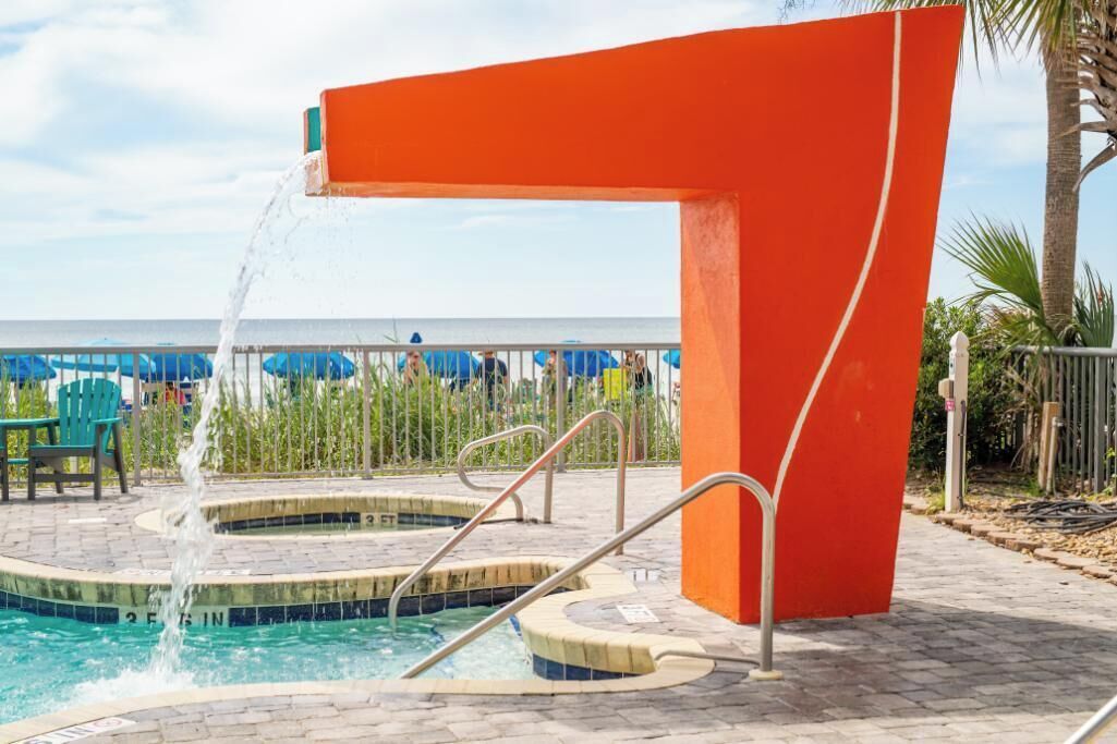 A pool area with a water feature, steps, and a view of the beach.