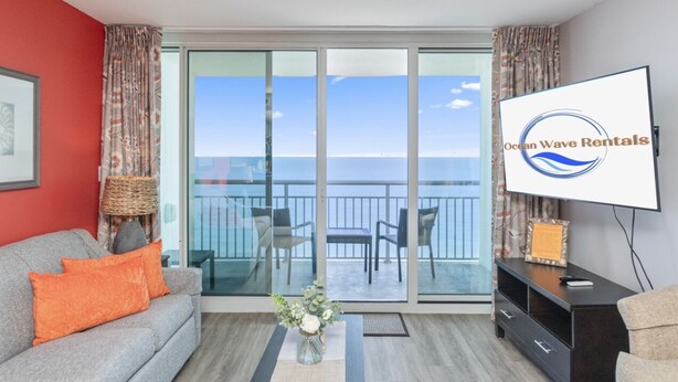 A room with a sofa, a TV, a table with a vase, and a balcony with a view of the ocean. - Amazing Oceanview Condo on the 17th Fl- 2 Balconies (Myrtle Beach)