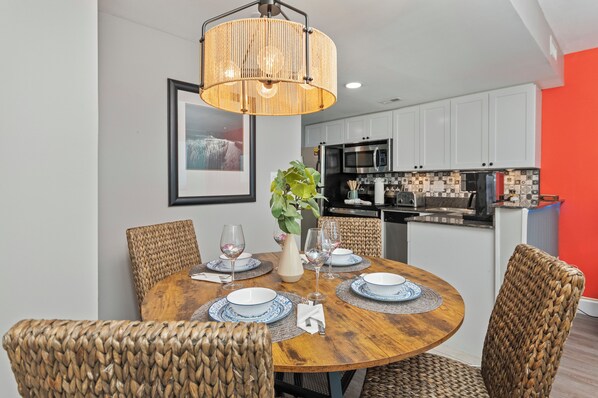 A dining area with a round wooden table, wicker chairs, and a hanging light fixture.