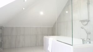 Een moderne badkamer met een douchecabine van glas, een witte badkuip en een betegelde vloer.