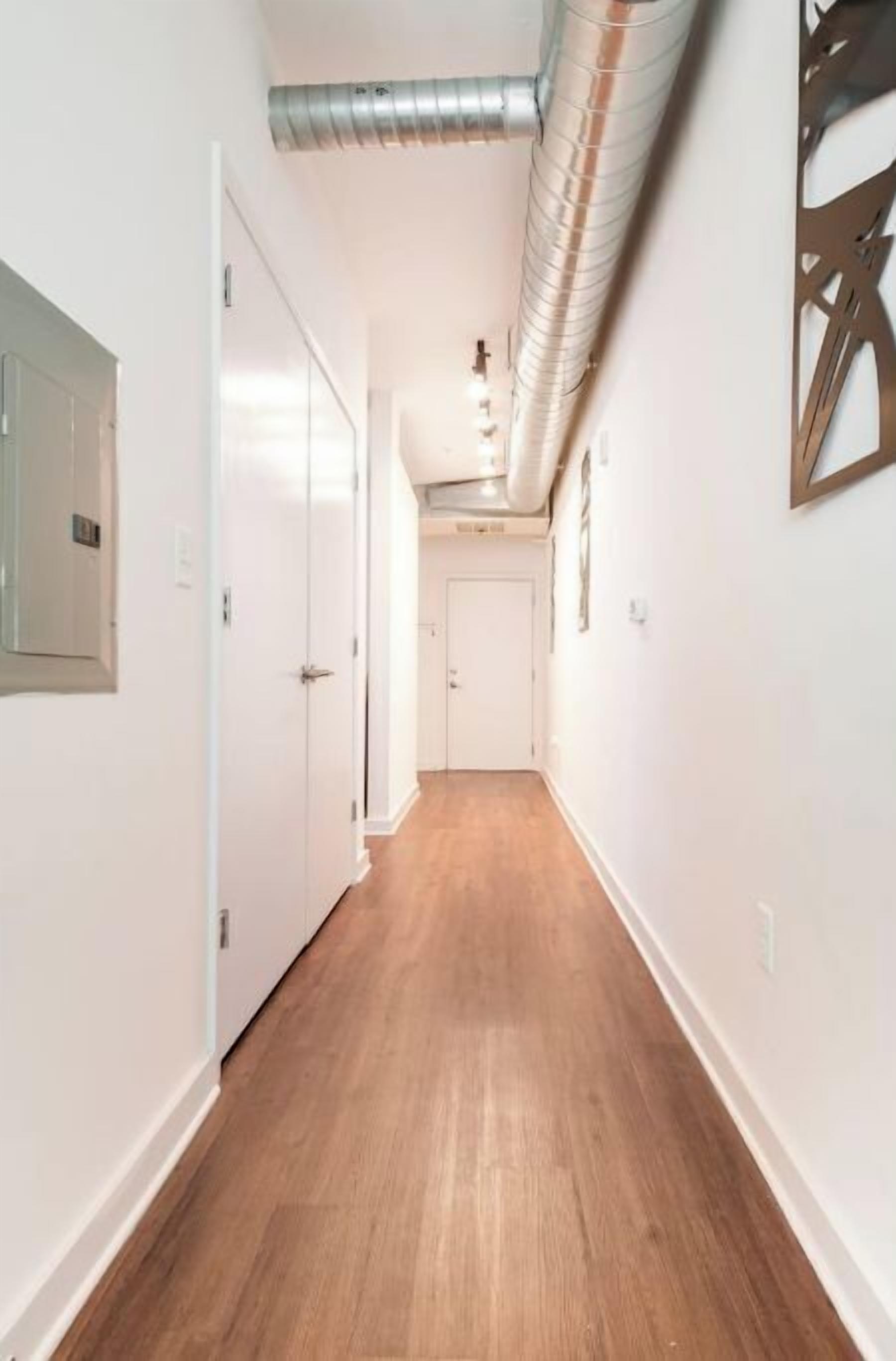 Un corridoio con pavimento in legno, pareti bianche e una bocchetta di ventilazione sul soffitto.