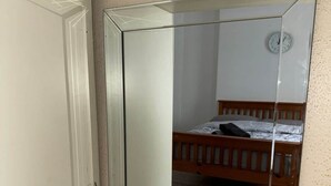 Une pièce avec un grand miroir, un lit en bois et une horloge au mur.