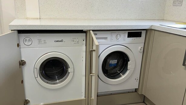 Une petite buanderie équipée de deux machines à laver à chargement frontal, d’un plan de travail et d’un pare-feu en carreaux.