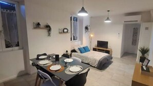 Ein modernes Apartment mit Essbereich, einem Bett mit blauem Kissen, einem Fernseher und einem kleinen Tisch mit einer Pflanze.