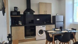 Eine kompakte Küche mit Waschmaschine, Mikrowelle und Kühlschrank. Ein Esstisch mit Stühlen steht bereit.