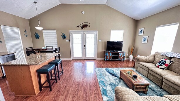 A spacious living area with a kitchen, wooden flooring, a large window, a ceiling fan, and a cozy seating area with a couch and a coffee table. - Creekside Getaway perfect for a relaxing weekend of fishing on the creek! (Sargent)