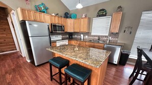 A kitchen with wooden cabinets, a granite countertop, a refrigerator, a microwave, an oven, a dishwasher, and a bar area with stools. - Creekside Getaway perfect for a relaxing weekend of fishing on the creek! (Sargent)