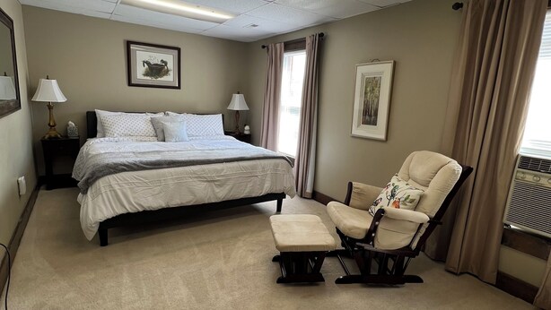 A hotel room with a bed, a chair, a nightstand, a lamp, and a window with curtains. - The Treehouse
 (Dayton)