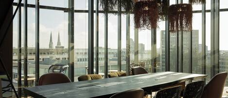 A modern conference room with a long table and chairs, large windows offering a city view.
