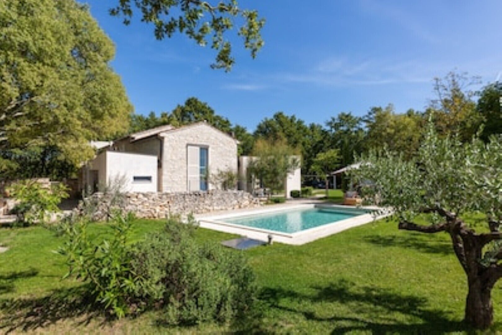 Una casa de piedra con piscina, rodeada de follaje y árboles.