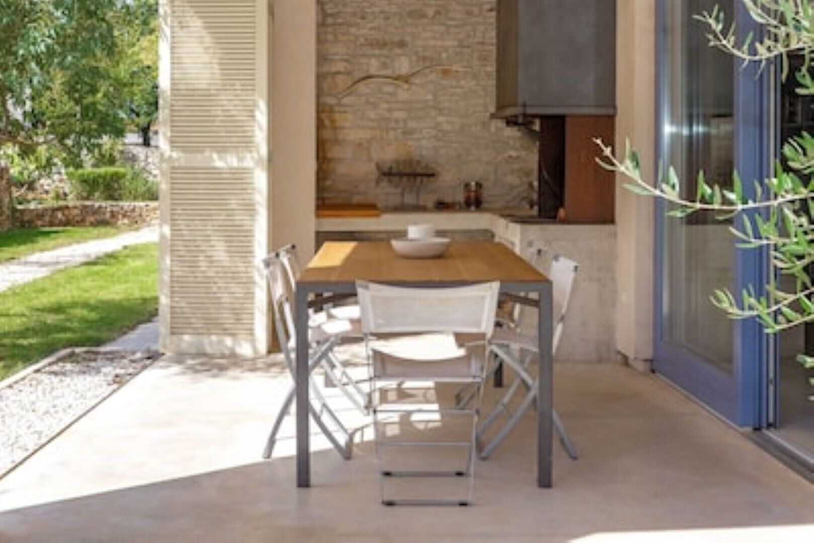 An outdoor dining area with a stone wall backdrop, a wooden table, and metal chairs.