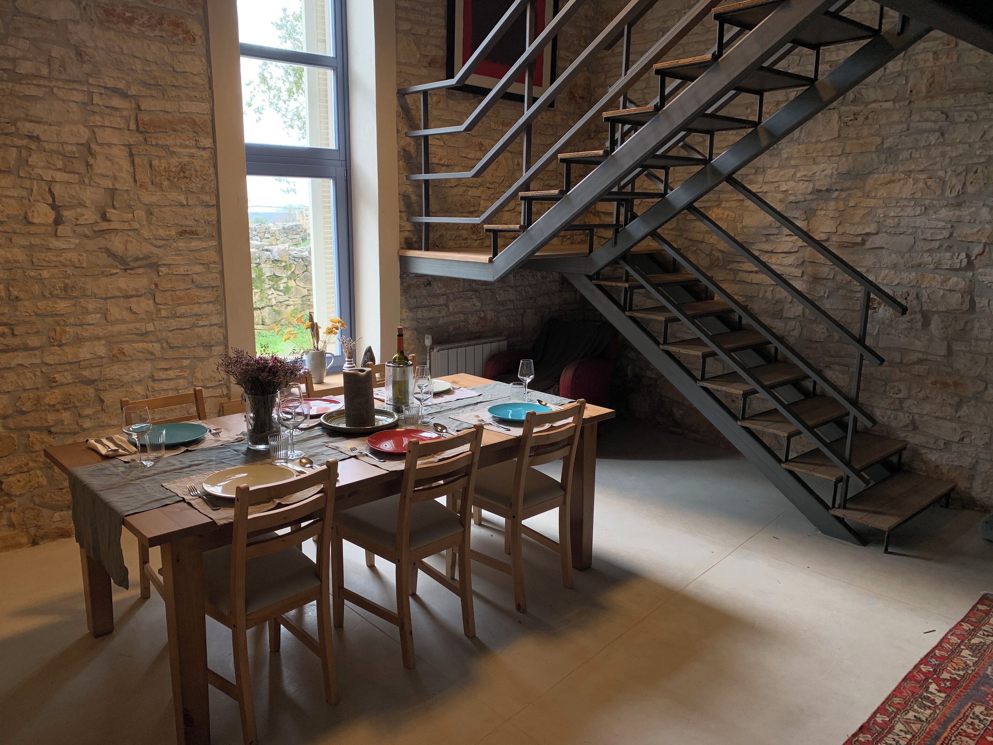 A dining area with a stone wall, a large window, and a staircase with metal railings.