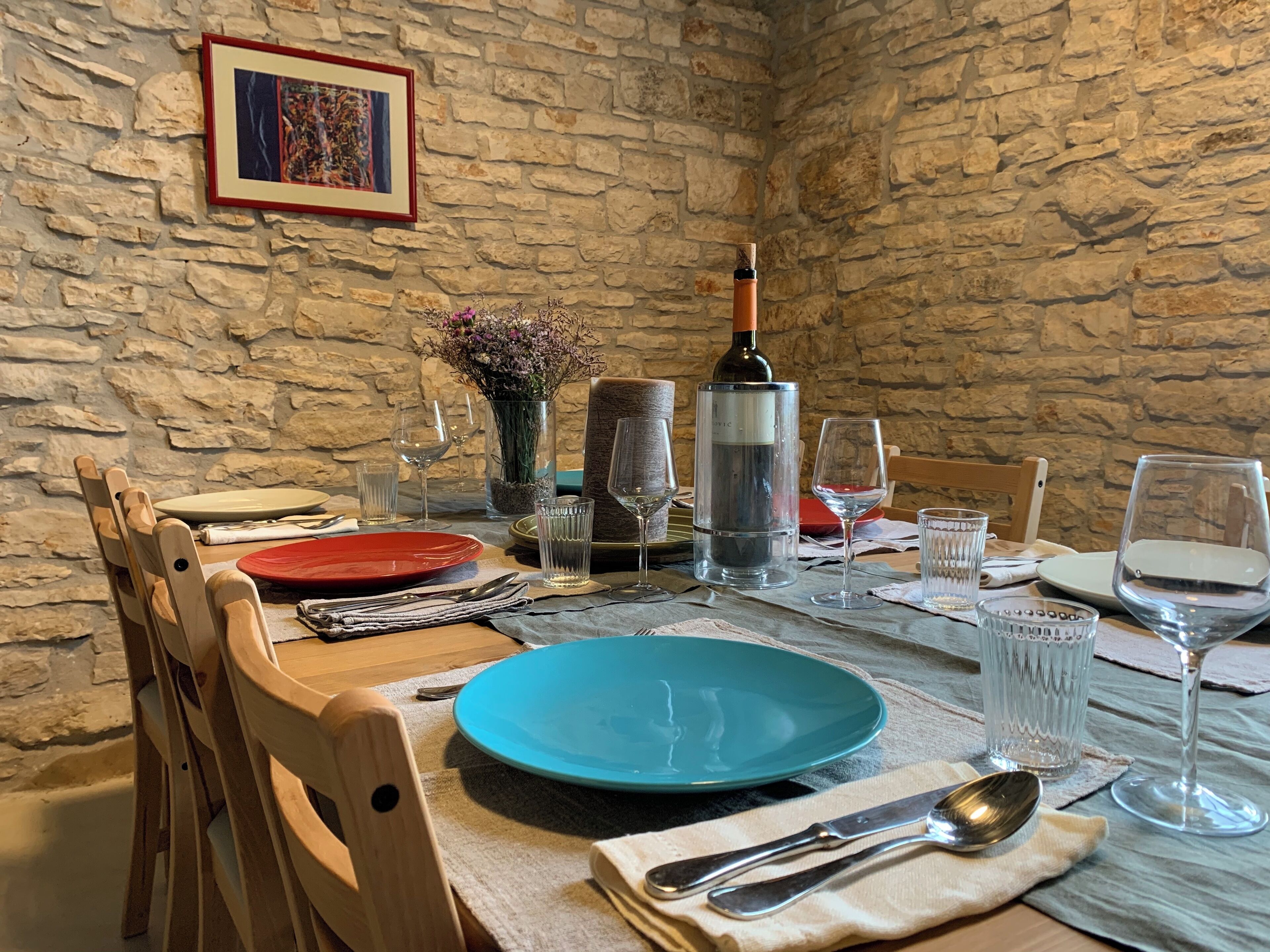Mesa lista con platos, vasos, cubiertos y una botella de vino en una habitación con paredes de piedra.