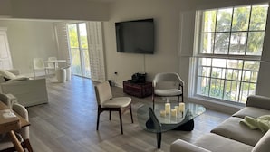 Ein geräumiges Wohnzimmer mit einem Glastisch, einer Couch und einem an der Wand befestigten Fernseher.