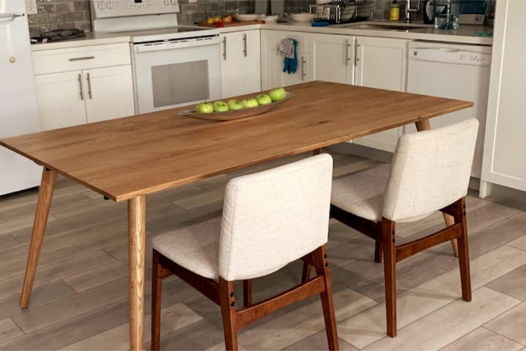 A kitchen with a wooden table, two chairs, and a bowl of green apples.