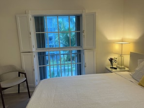A hotel room with a bed, a chair, a nightstand with a lamp, and a window with a view of palm trees. - Key Biscayne 2 bedrooms sleeps 4 walk 2 beach shops (Key Biscayne)