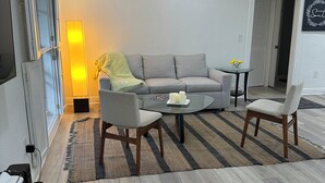 Ein modernes Wohnzimmer mit einem grauen Sofa, zwei Sesseln, einem Glastisch und einem Streifenmuster-Teppich.