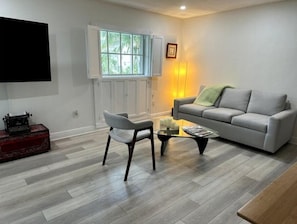 A living room with a grey sofa, a white armchair, a coffee table, and a television mounted on the wall.