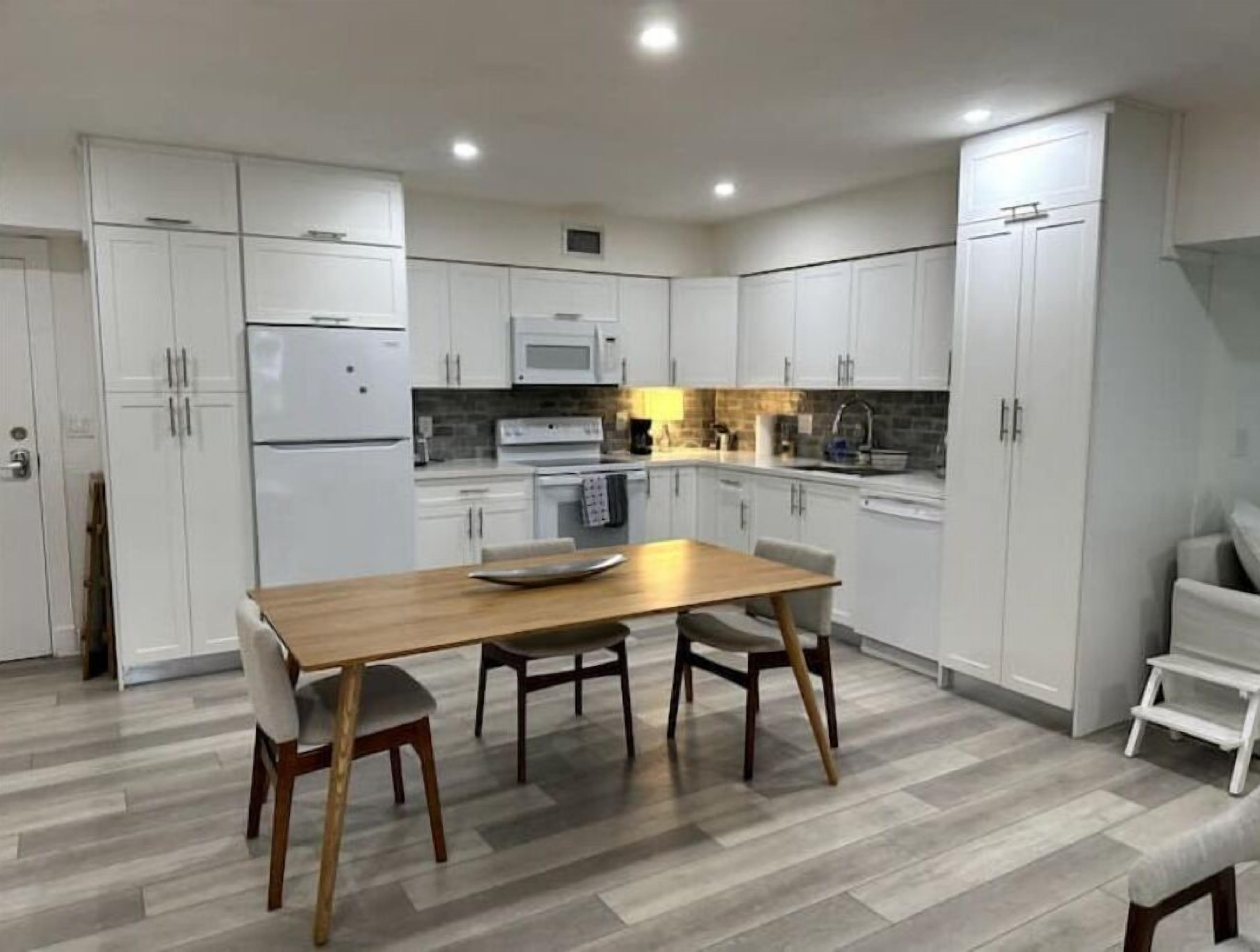Cozinha moderna com armários brancos, uma mesa de jantar de madeira e painel de azulejos.