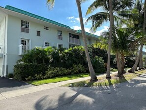 A two-story building with a green roof, surrounded by lush greenery and palm trees.