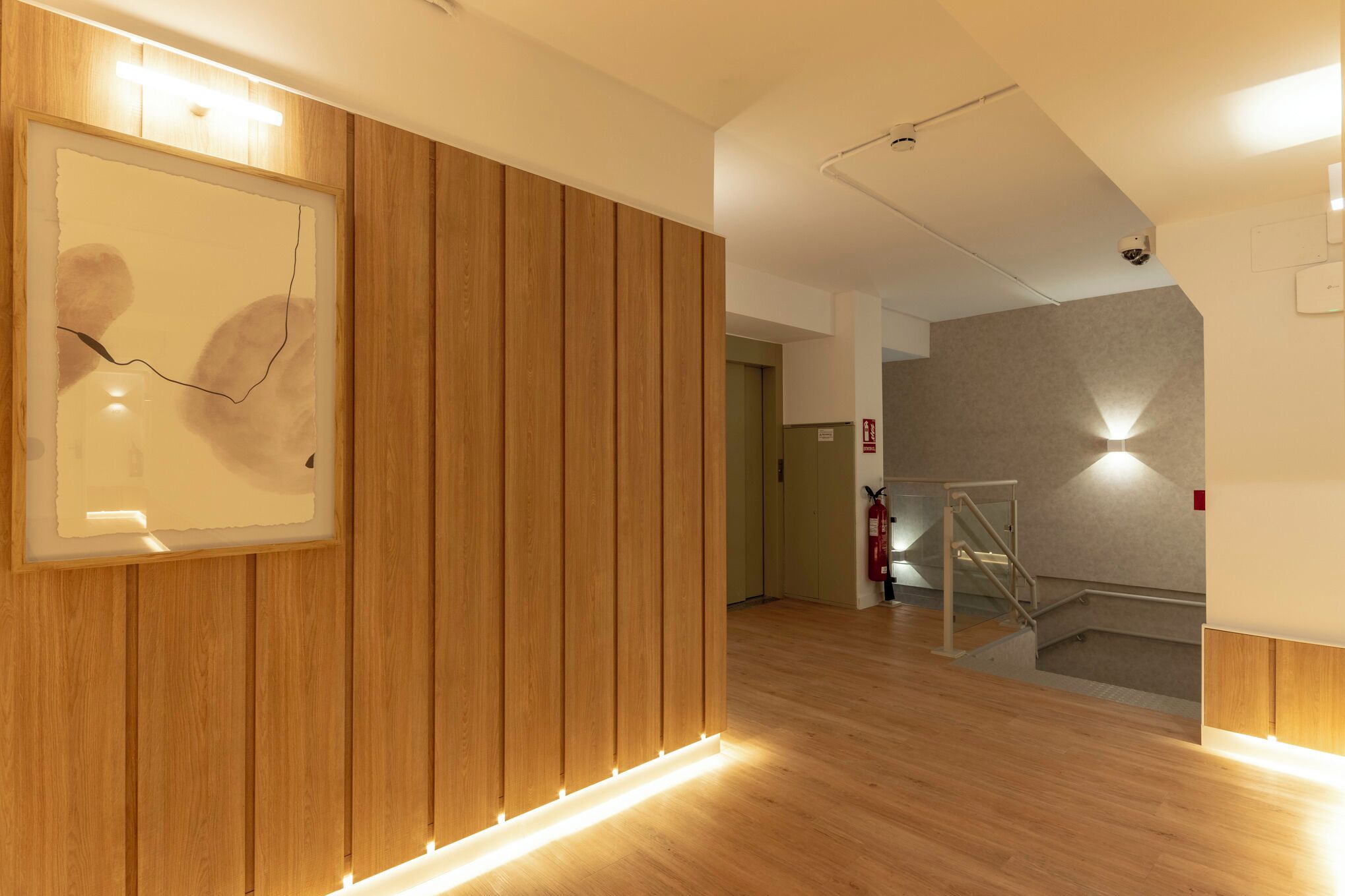 Un interior modern amb panells de fusta, una obra d'art abstracta emmarcada i una escala amb barana metàl·lica.