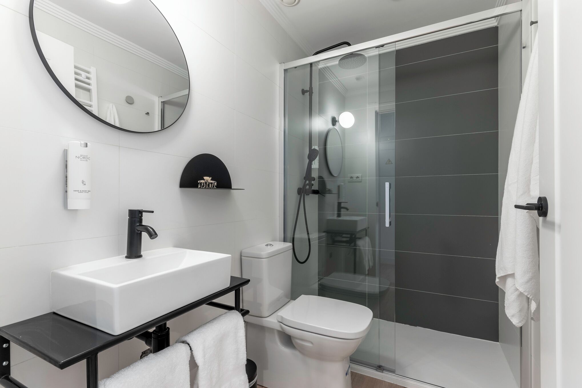 Een moderne badkamer met een witte wastafel, een zwart aanrechtblad en een douche met glazen wanden.