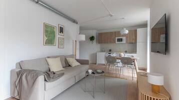 Uma sala de estar moderna com sofá, mesa de centro e área de jantar com cadeiras e mesa. Cozinha visível ao fundo, com micro-ondas e armários.
