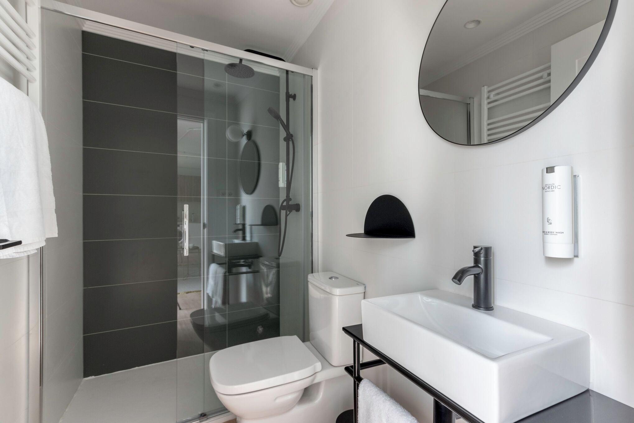 A modern bathroom with a glass shower enclosure, a white toilet, a sink with a black faucet, and a mirror.
