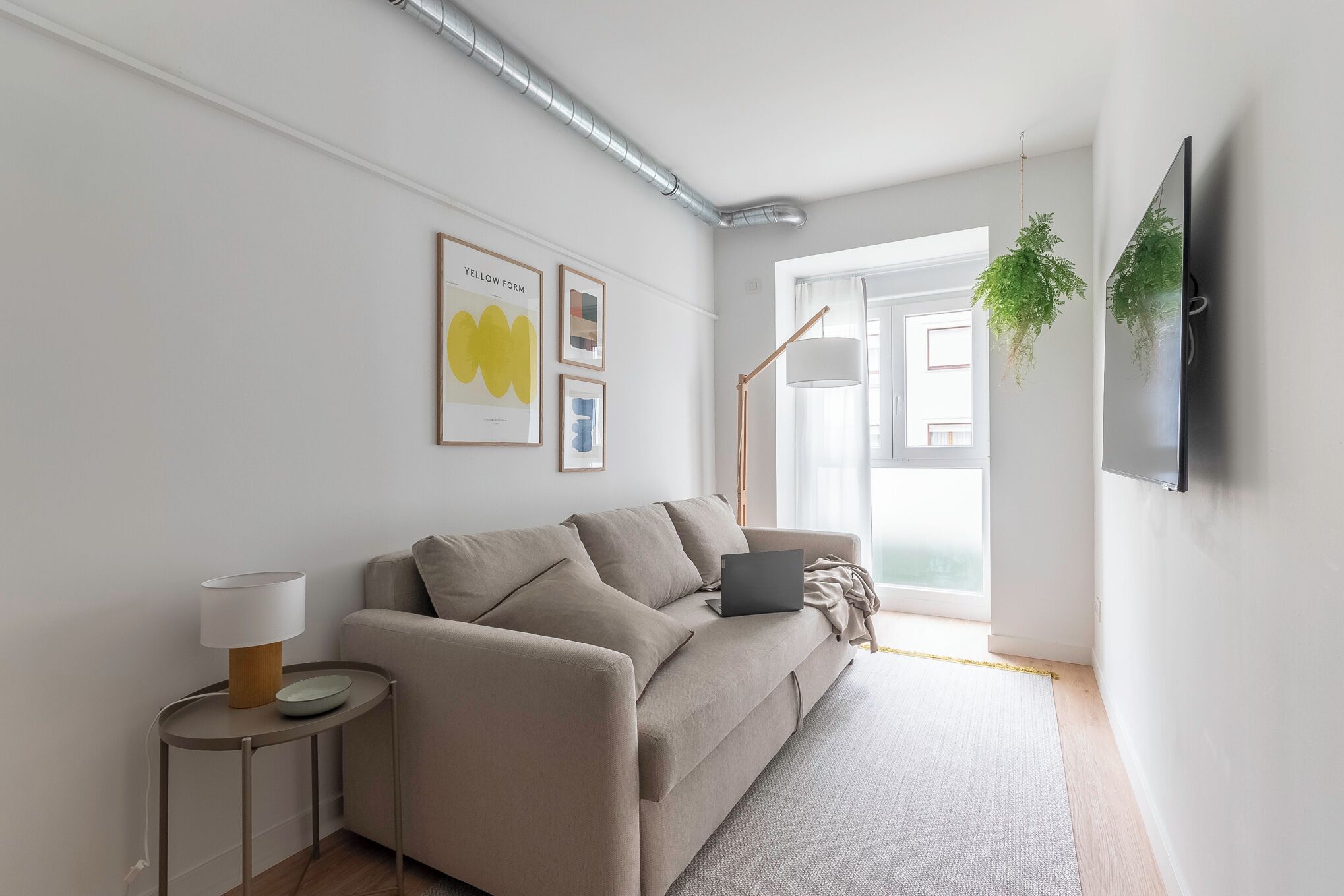 A modern living room with a sofa, a side table, a lamp, and a wall-mounted TV.