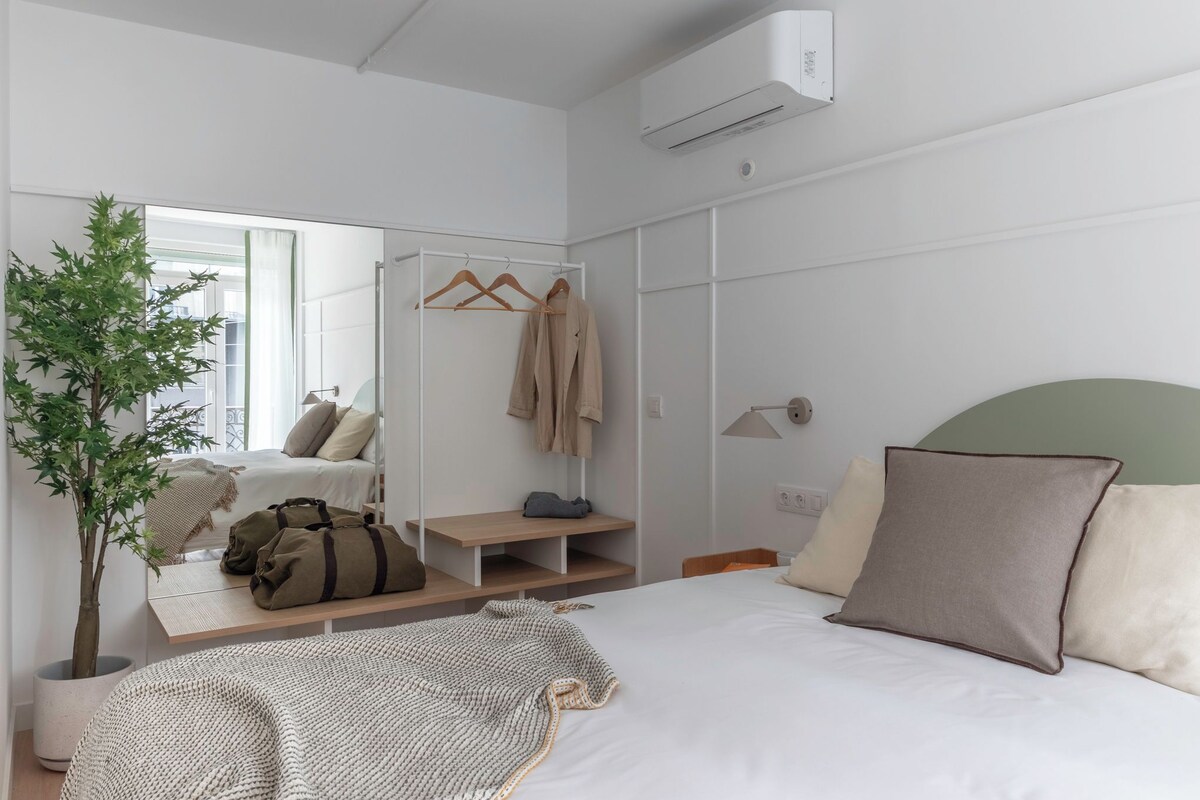 A modern bedroom with a bed, a mirror, a wardrobe, a bedside table, and a potted plant.
