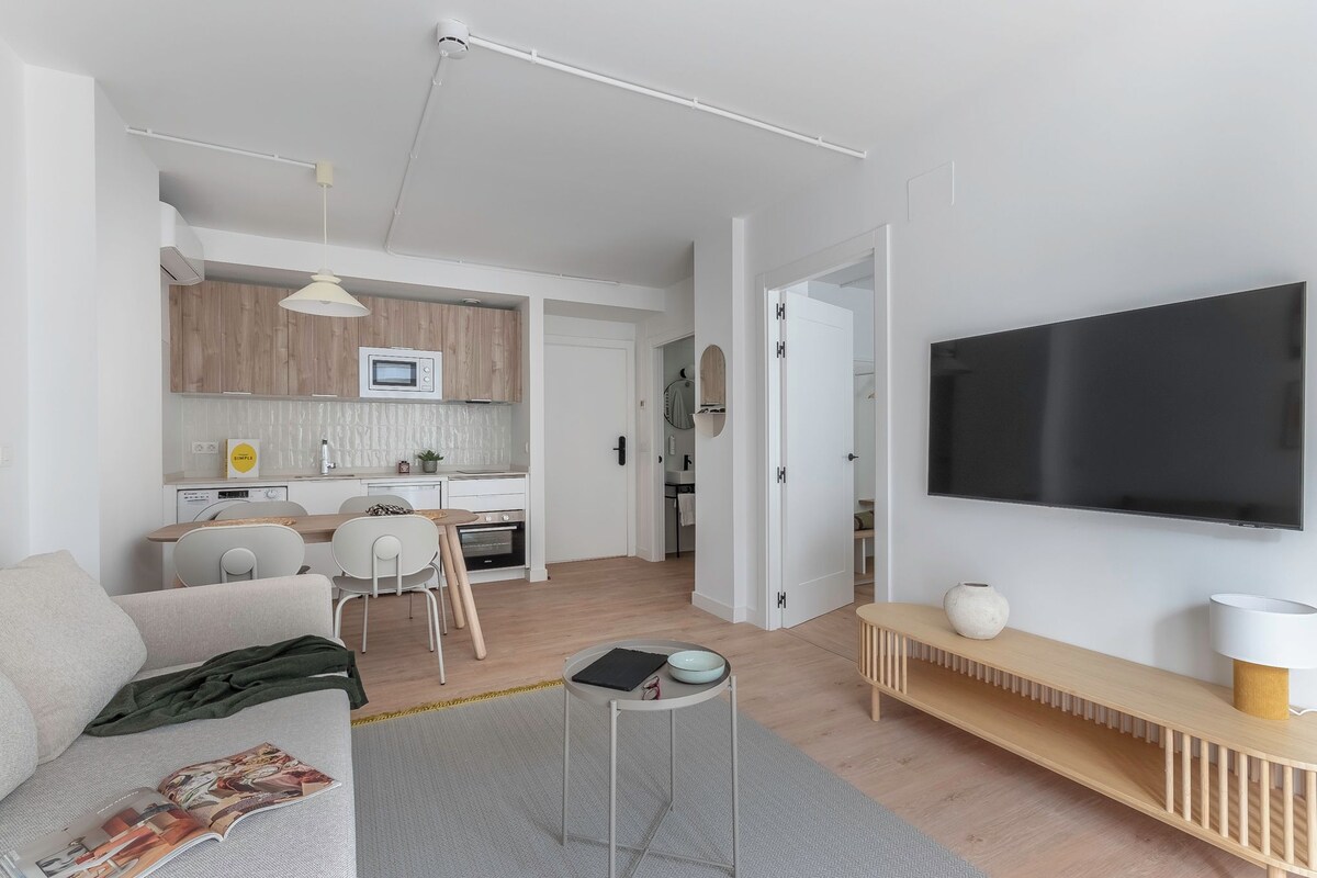 A modern living room with a sofa, a coffee table, a TV, and a kitchen area in the background.