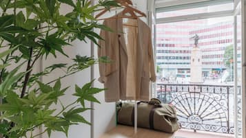 Una habitación con perchero, un banco con un bolso y vista a un paisaje urbano a través de una ventana.