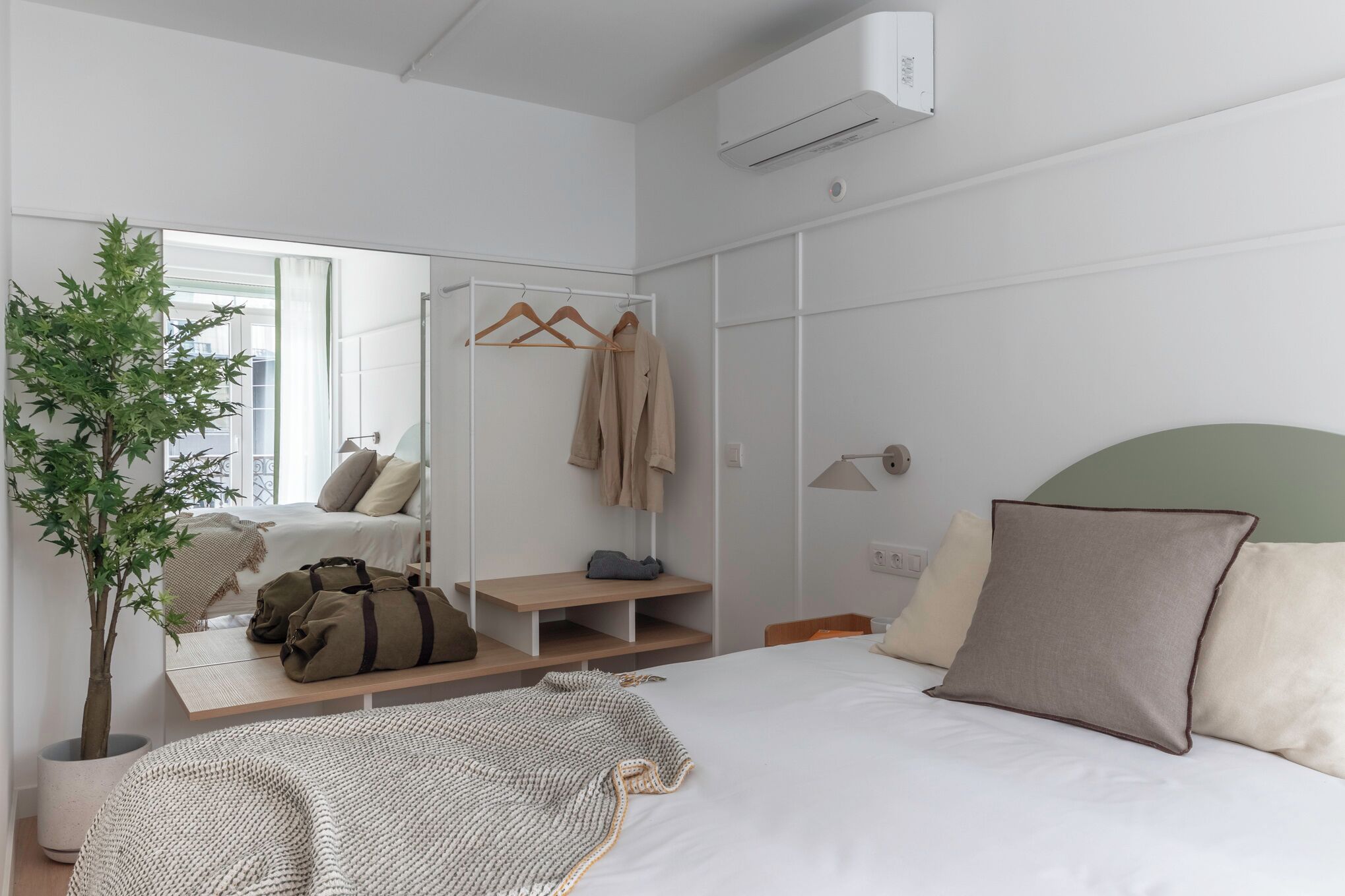 Um quarto moderno com uma cama, um espelho, um guarda-roupa, uma mesinha de cabeceira e um vaso de plantas.