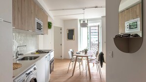 A modern kitchen with wooden cabinets, a built-in microwave, and a washing machine. There is a dining area with a table and chairs, and a large mirror on the wall. - B48 Bilbao Abando (Bilbao)