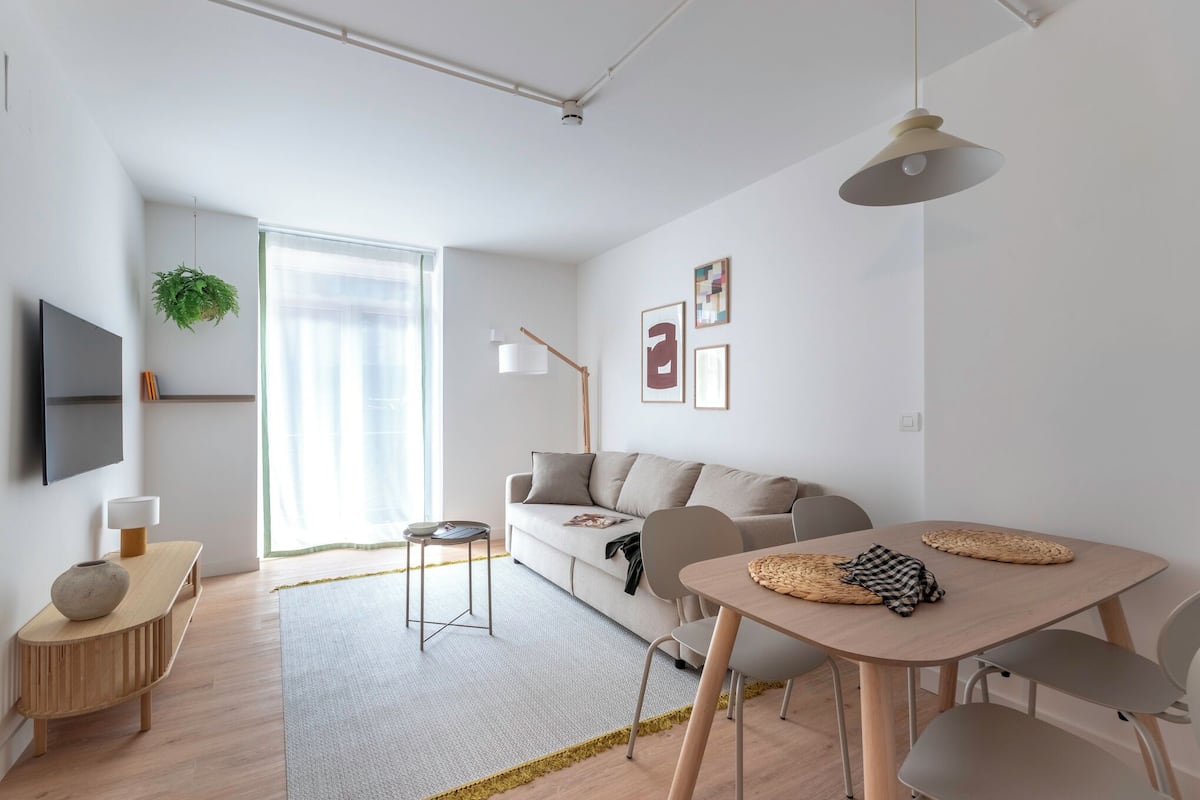 A modern living room with a sofa, a dining table, and a TV mounted on the wall.