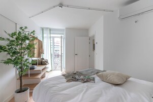 Camera da letto minimalista con un letto, una pianta in vaso e vista sull'esterno.