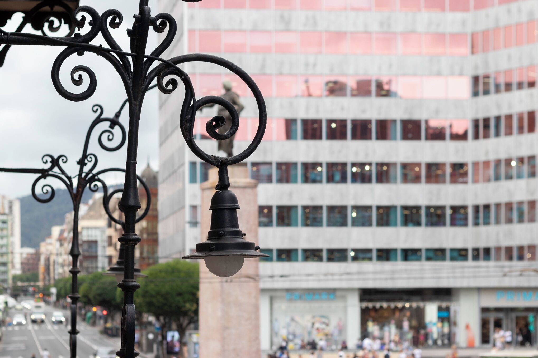 Vista de la calle con un edificio moderno, un farol y una estatua.