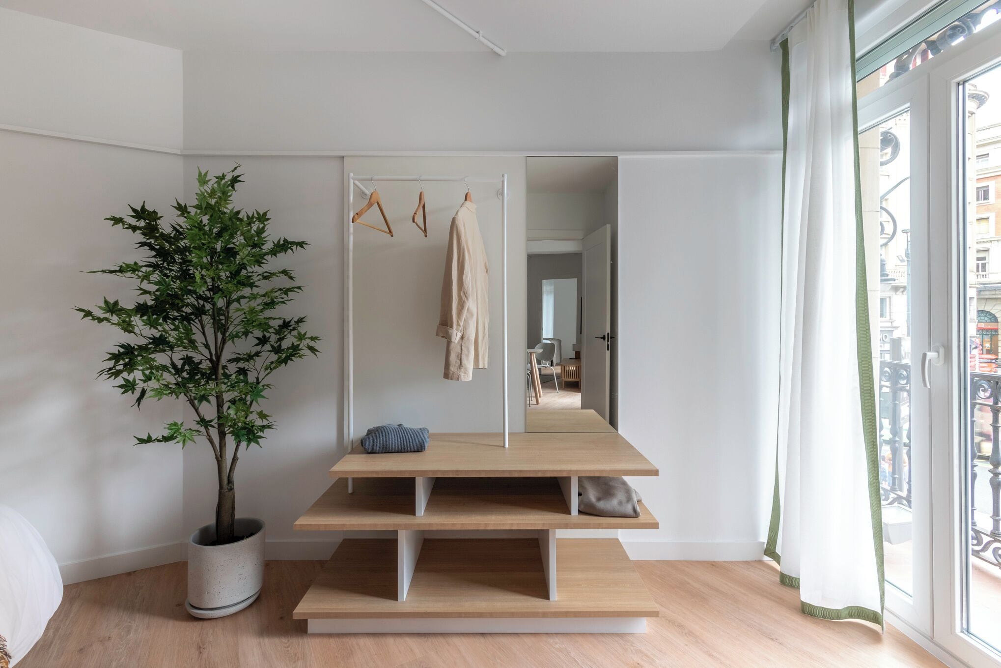 Habitación minimalista con un espejo grande, una planta y un banco.