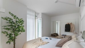 A hotel room with a bed, a bedside table, a lamp, a mirror, a wardrobe, and a potted plant. - B48 Bilbao Abando (Bilbao)