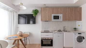 Una cocina moderna con horno empotrado, microondas y lavadora, un comedor con mesa y sillas, y un televisor de pantalla plana grande montado en la pared.