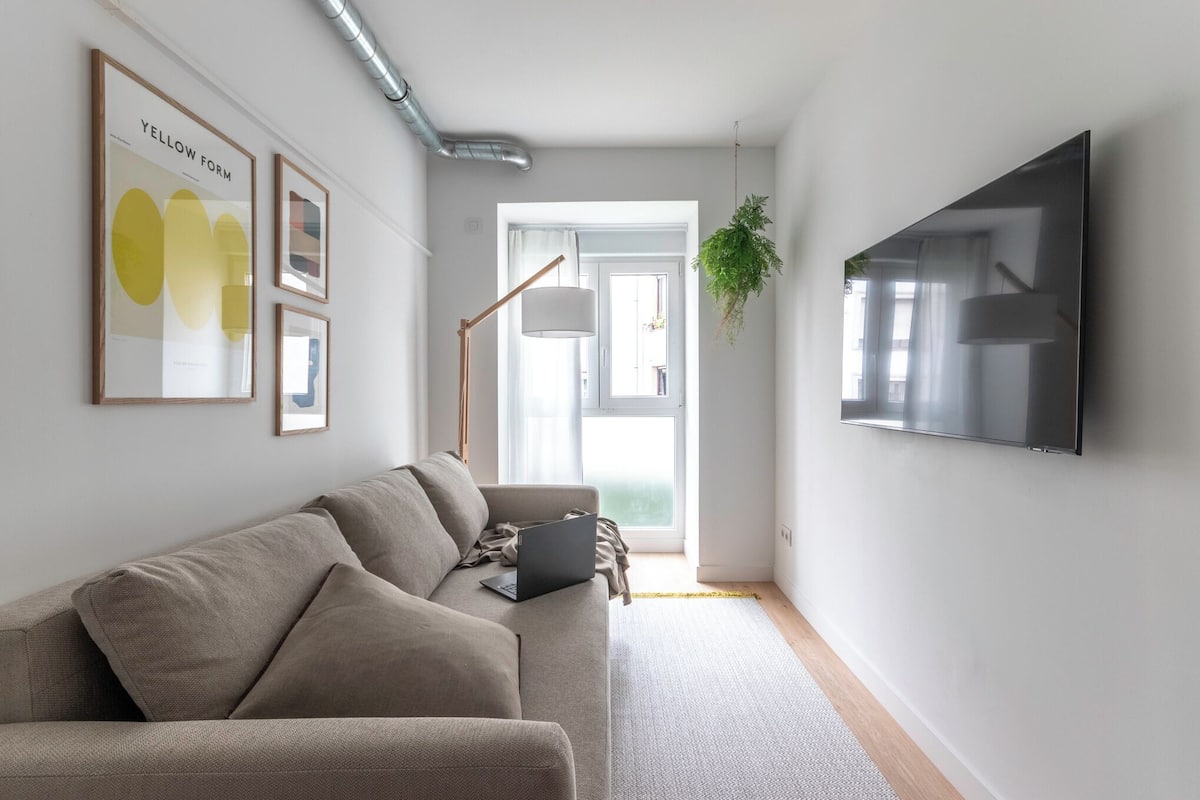 A modern living room with a sofa, a mounted TV, and framed artwork on the wall.